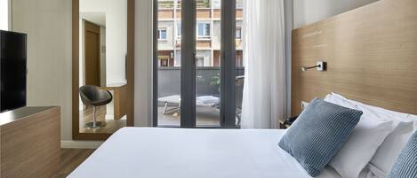 A hotel room with a large bed, a TV, a desk, and a sliding glass door to the balcony.
