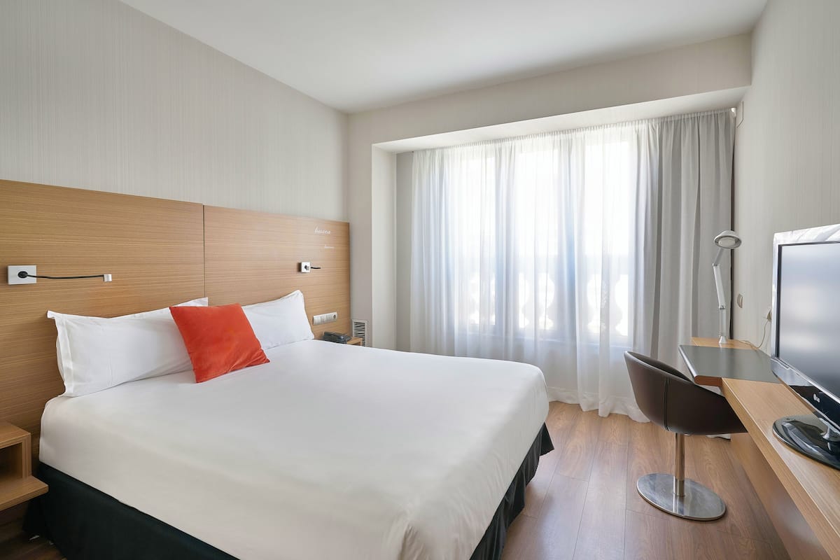 Een hotelkamer met een groot bed, een bureau met stoel, een televisie en een raam met gordijnen.