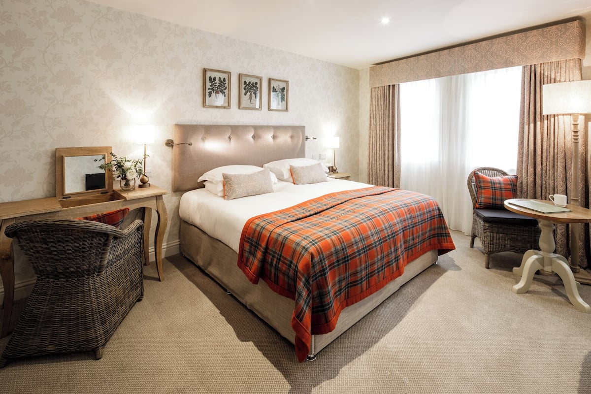 Une chambre d’hôtel avec un grand lit, une table de chevet avec une lampe, une chaise et une petite table avec une lampe.
