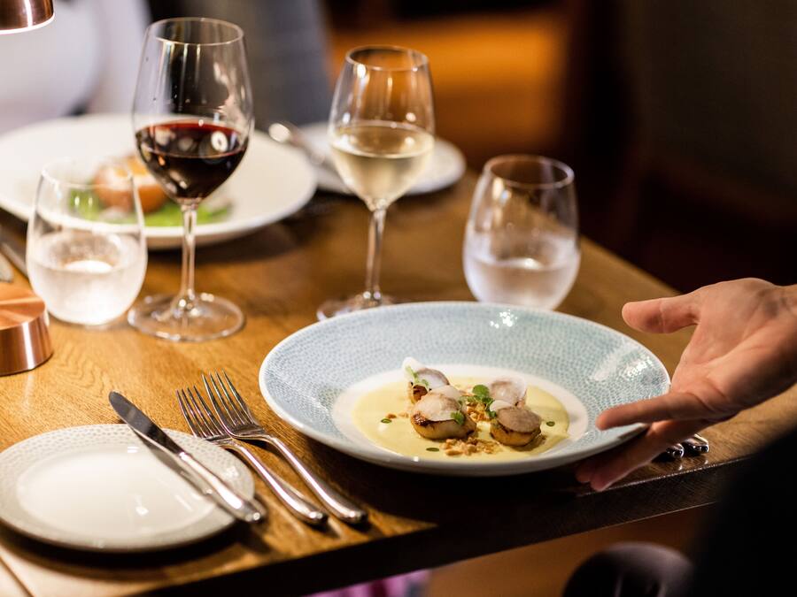 Una mesa de comedor con platos, cubiertos y copas de vino.