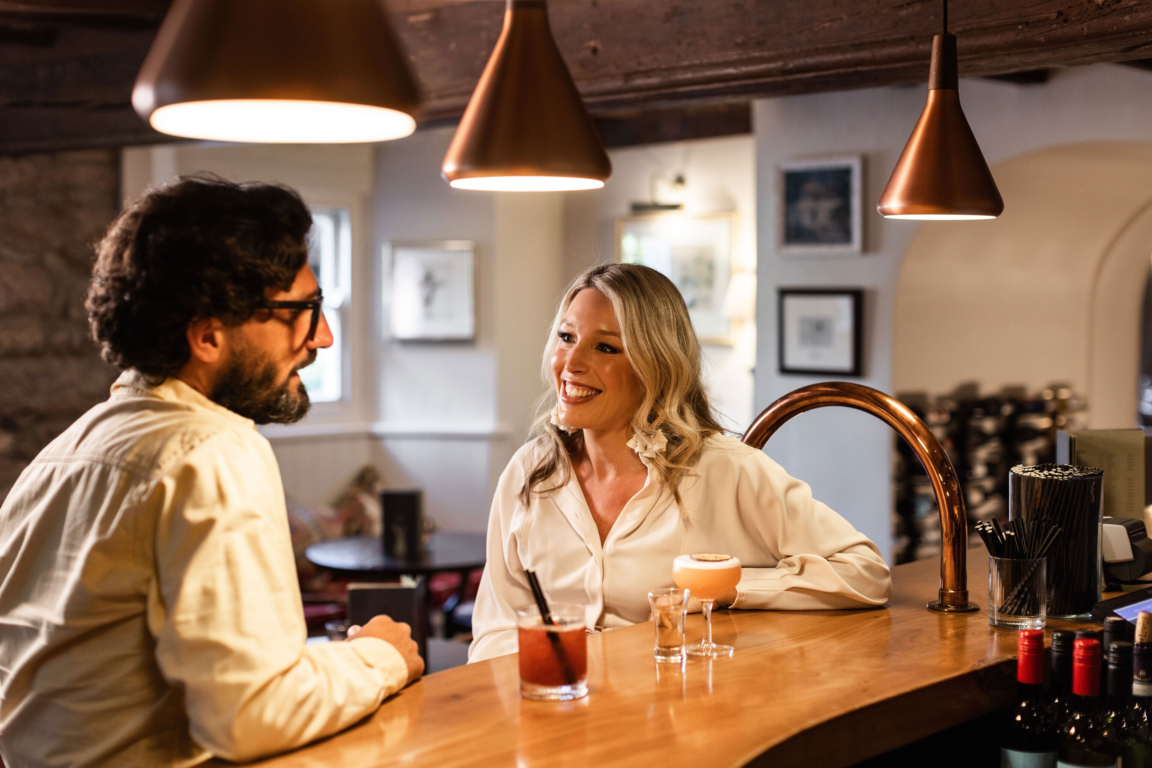 Un espace bar doté d’un comptoir en bois, de luminaires suspendus en cuivre et d’un présentoir à bouteilles de vin.