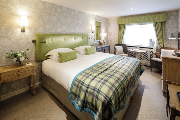 A hotel room with a large bed, a desk, a chair, a small table, and a window with curtains.