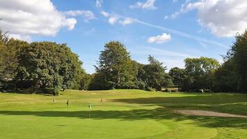 A golf course with multiple holes, trees, and a clear sky.