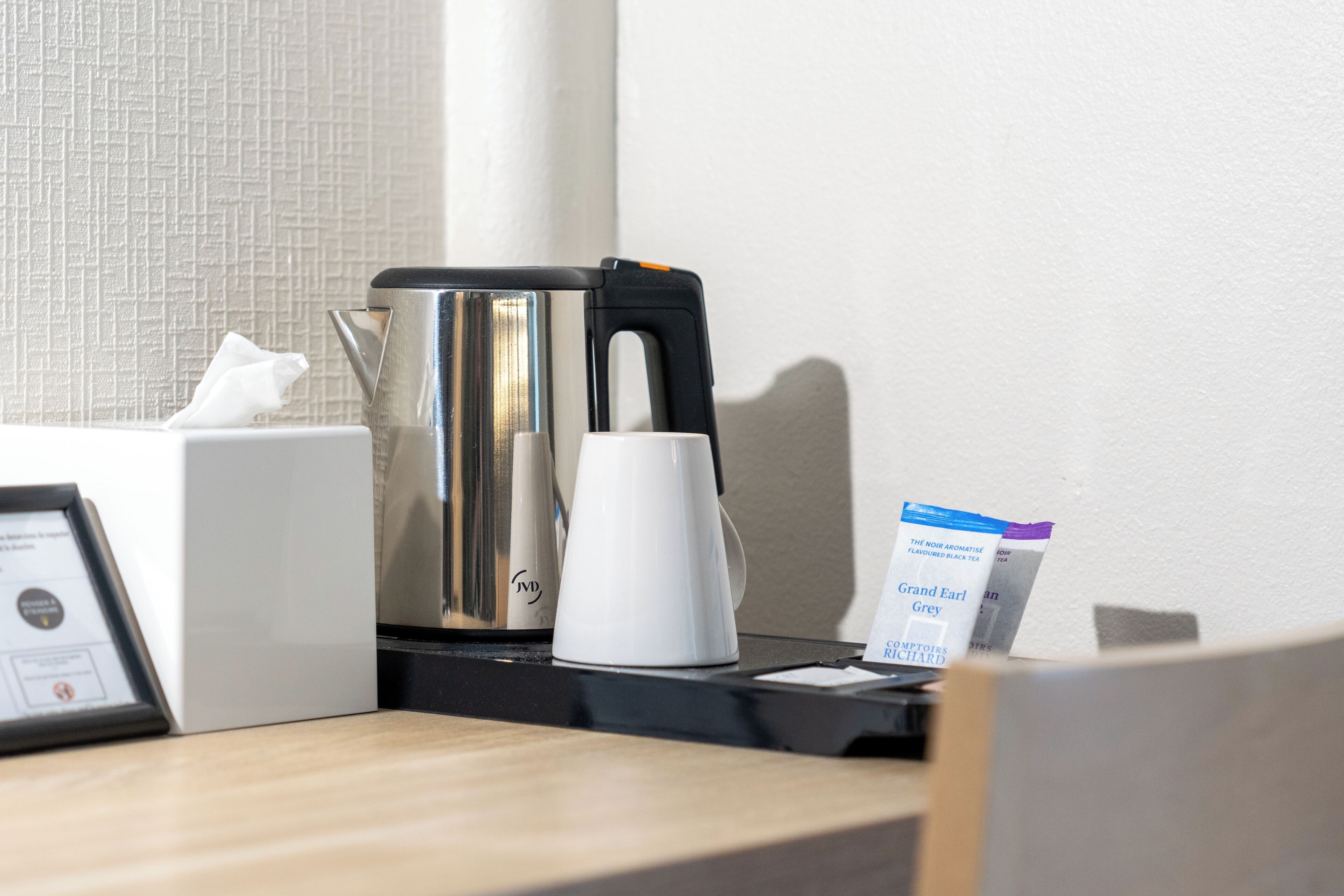 Una cafetera, una caja de pañuelos y una bolsita de té sobre una encimera de hotel.