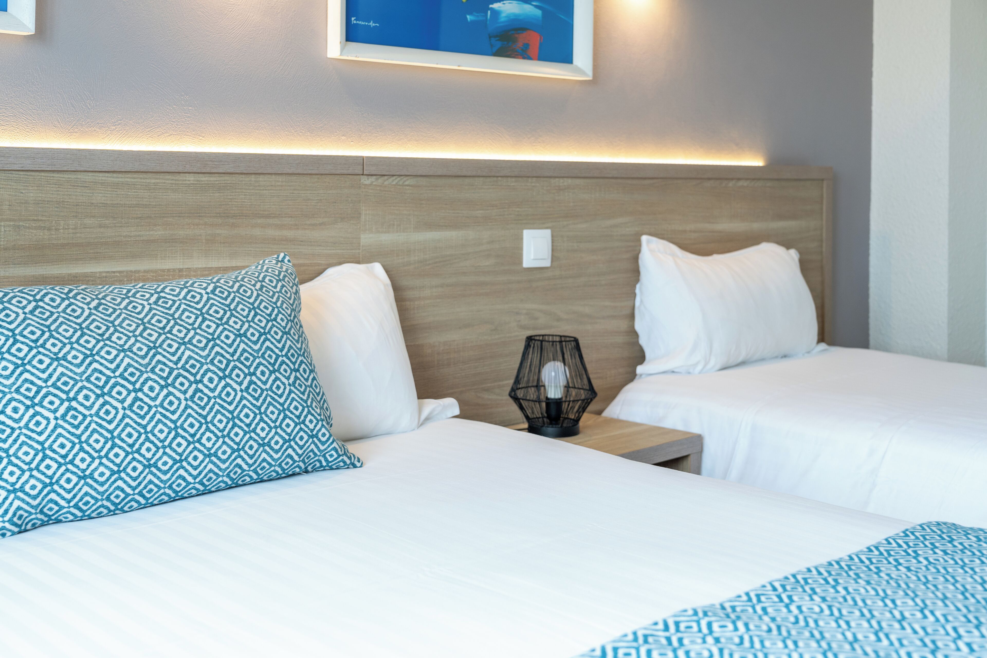 A hotel room with two beds, a nightstand with a lamp, and a wall-mounted picture.