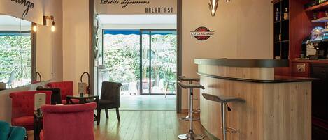 Un bar lounge con sillas rojas y negras, una barra de madera y una zona de desayuno con vistas a palmeras.