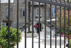 A stone building with a balcony, outdoor seating, and a staircase. - Hotel Ariane (Pontorson)