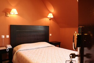 Habitación de hotel con una cama grande, dos lámparas de noche, una mesita de noche con un teléfono y una pequeña mesa.