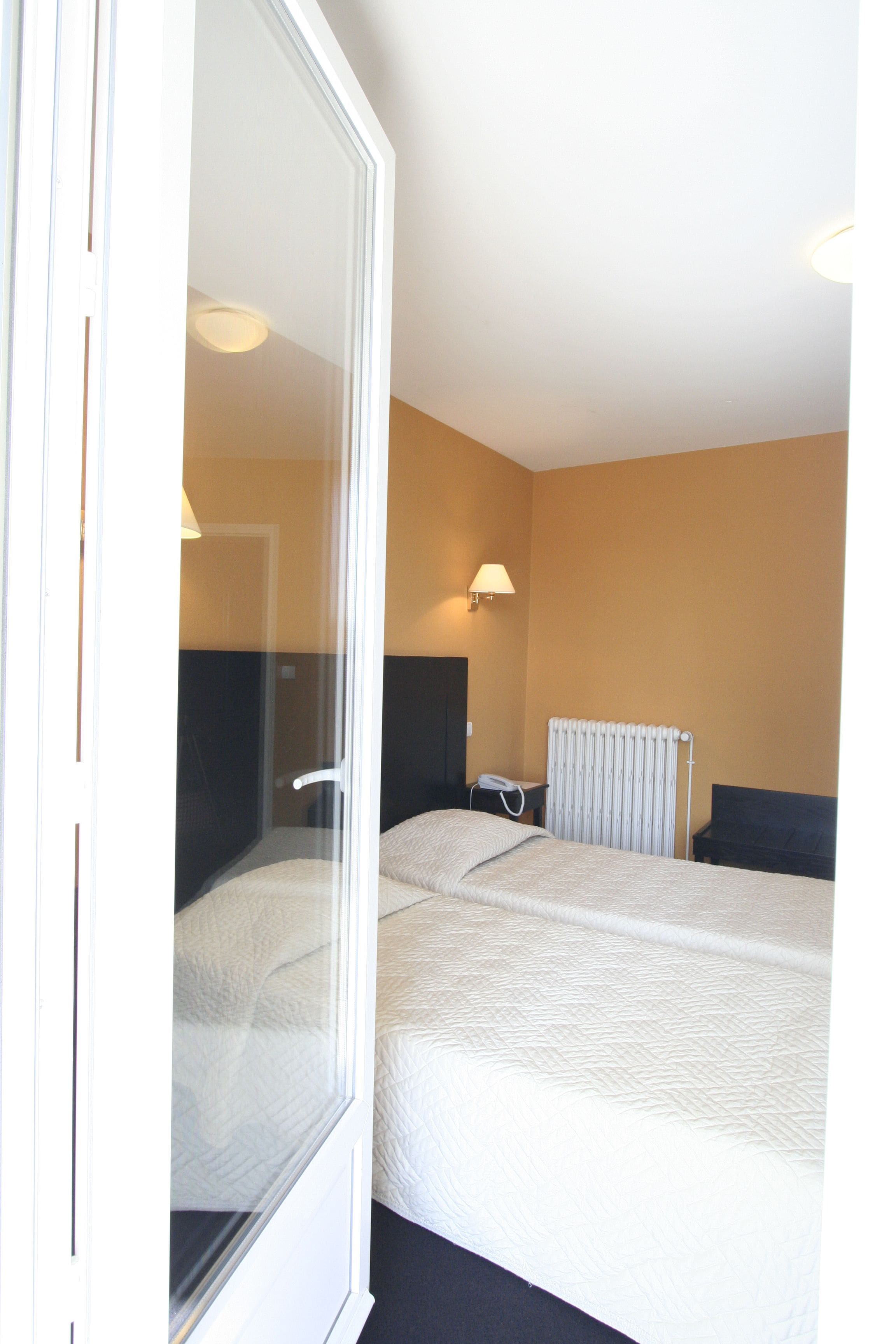 Habitación de hotel con dos camas, un radiador, un teléfono y una lámpara fijada a la pared.