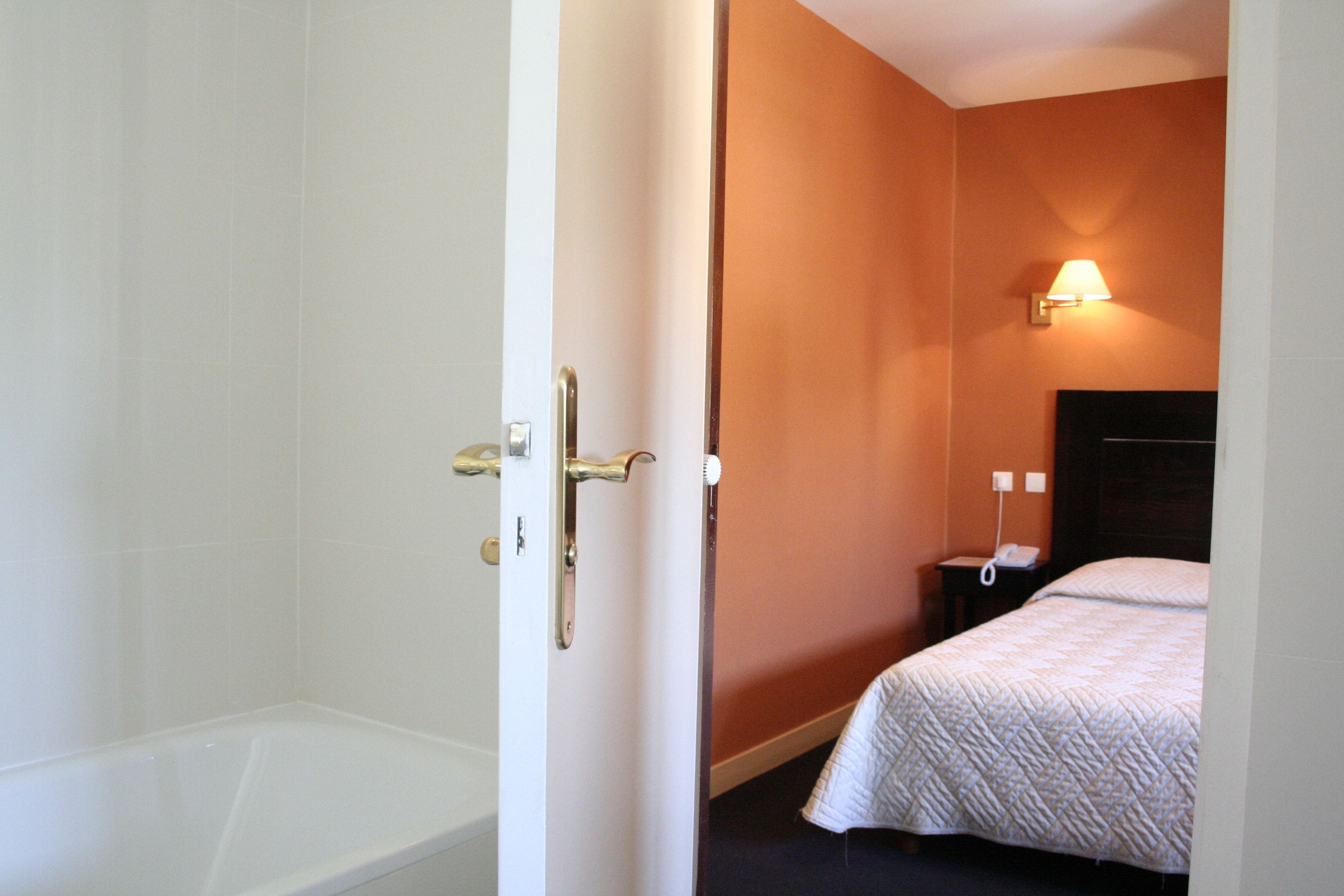Una habitación de hotel con una bañera, una cama con colcha blanca y una mesita de noche con lámpara.