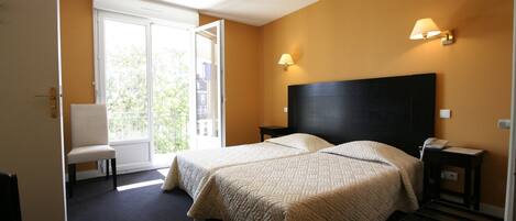 A hotel room with two beds, a chair, a desk, and a window with a view of greenery.