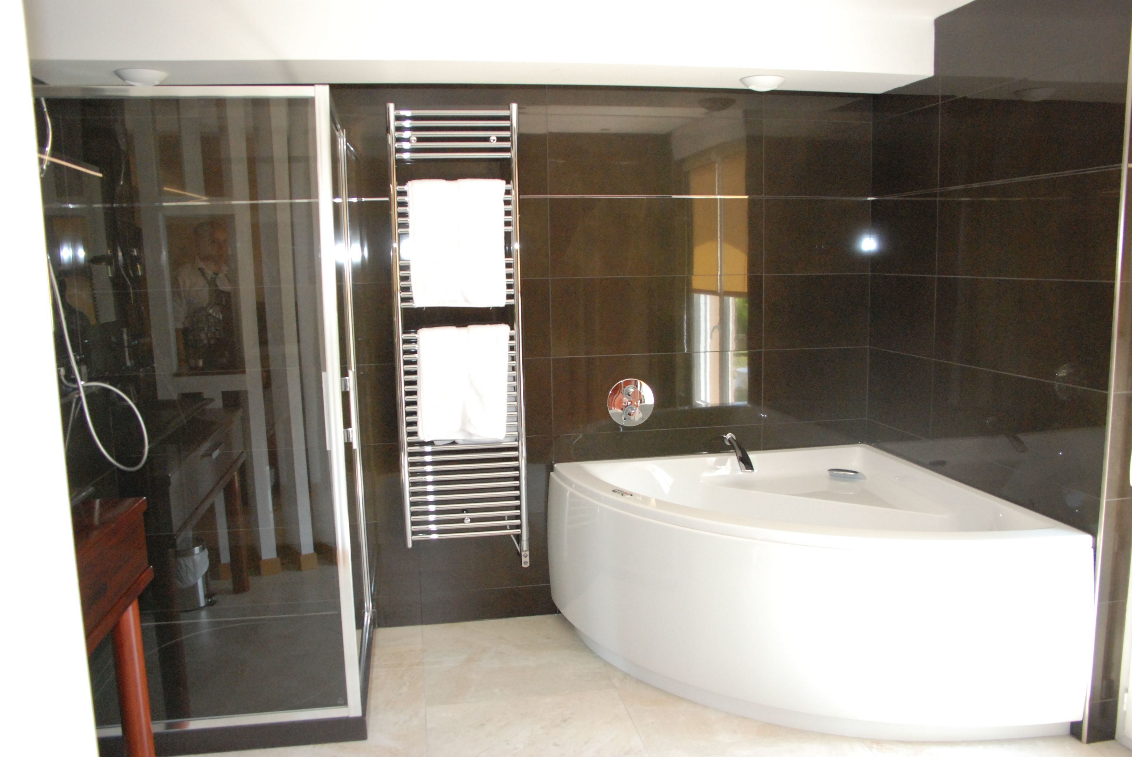 Een moderne badkamer met een ruime badkuip, een douchecabine van glas en een donkere betegelde wand.