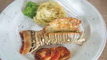 Une assiette comprenant une queue de homard, des spaghettis et des tomates grillées.