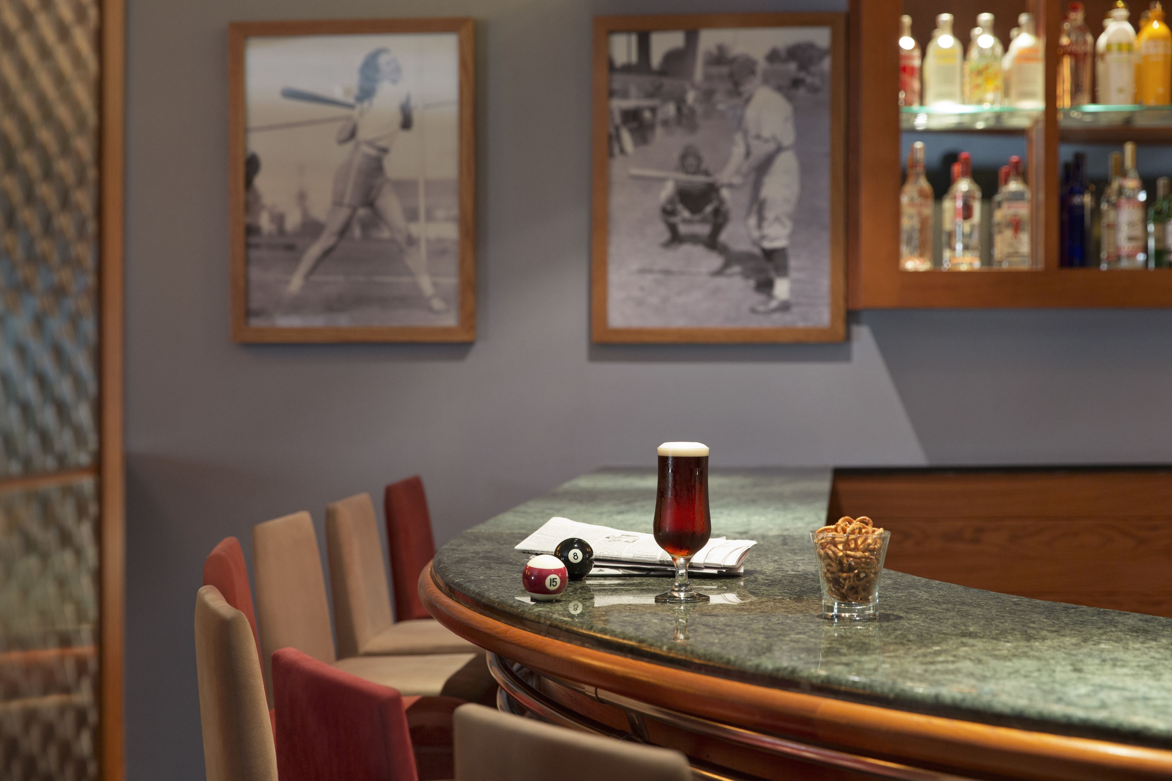 A bar area with a round table, chairs, framed pictures on the wall, and bottles on shelves.