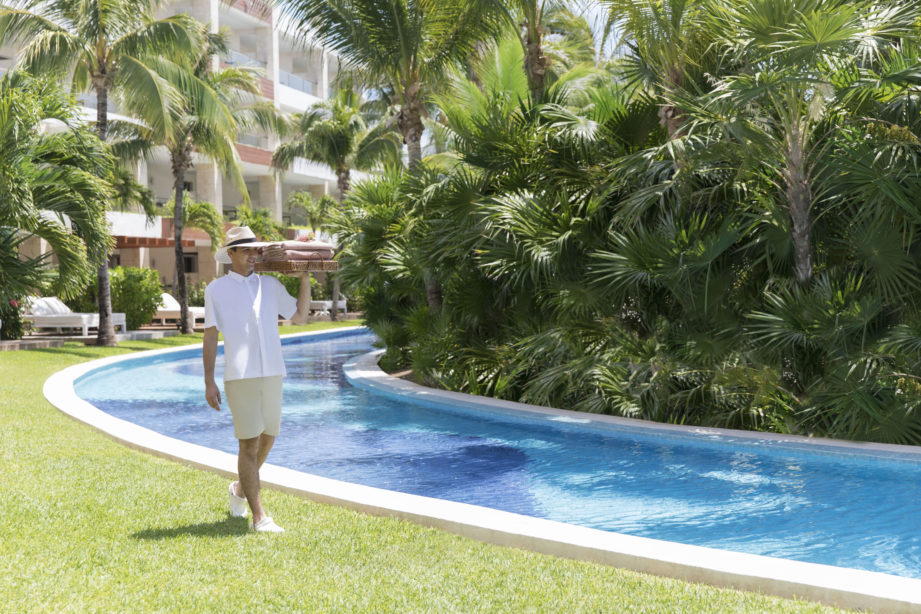Un homme se promène le long d’une piscine, avec des palmiers et un bâtiment en arrière-plan.