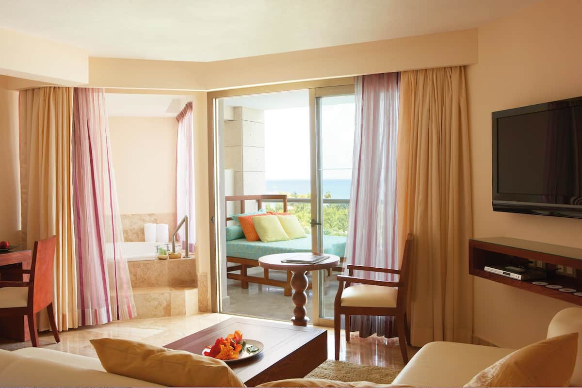 A hotel room with a balcony, a TV, a dining table, and a sofa.