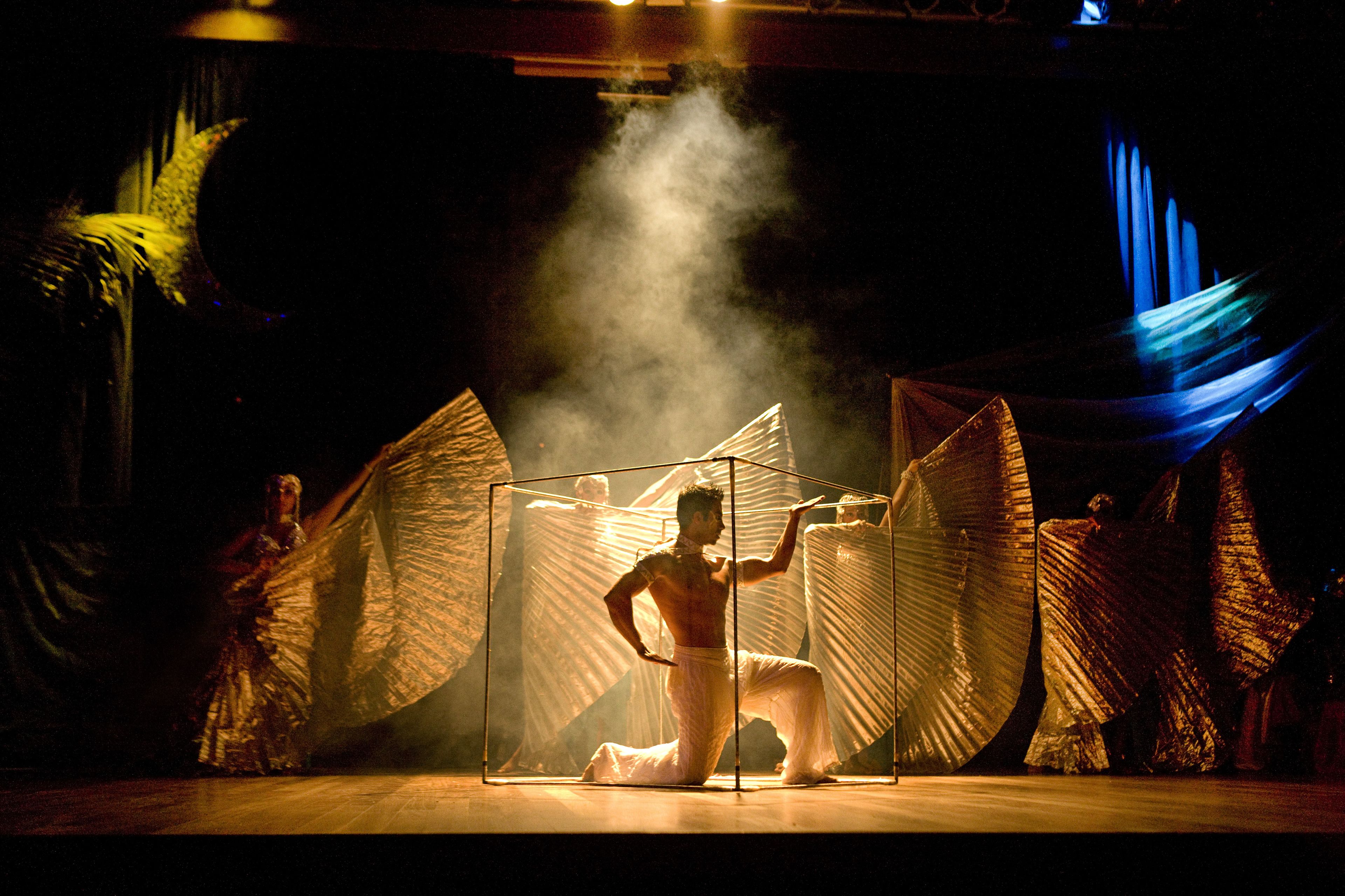 A stage with a performer in a white outfit, surrounded by large, illuminated wings.