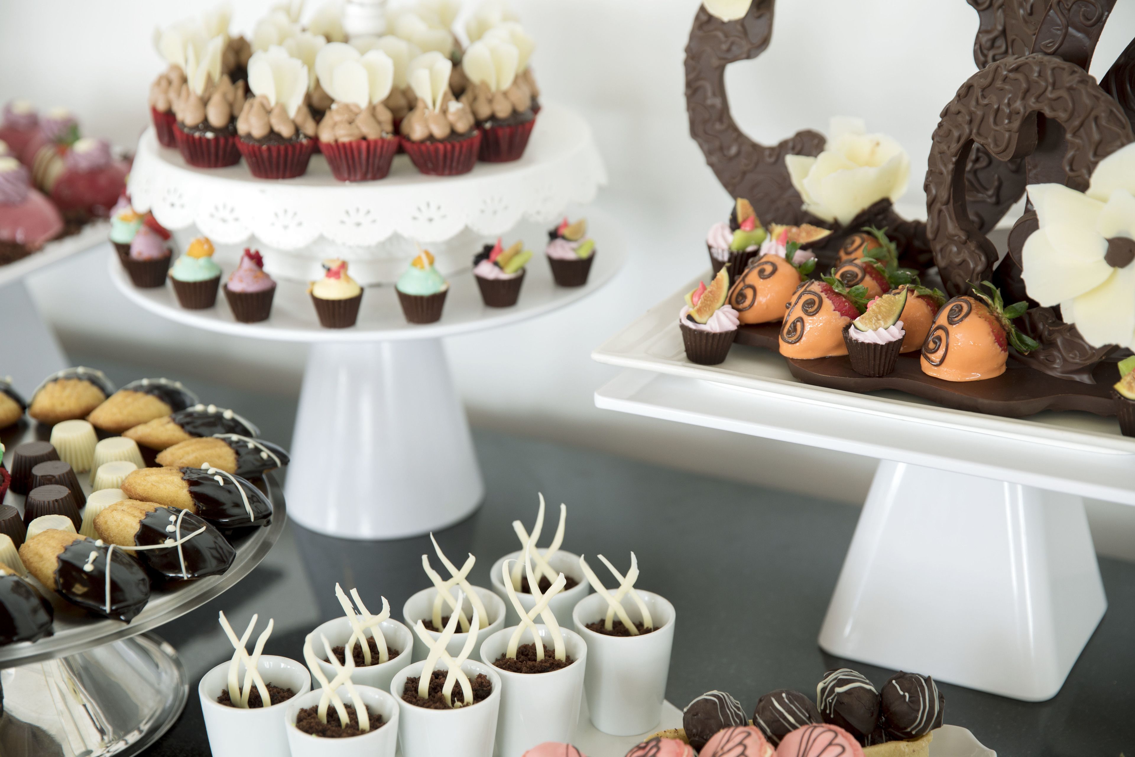 Une présentation de desserts comprenant divers cupcakes et chocolats, disposés sur des présentoirs blancs.