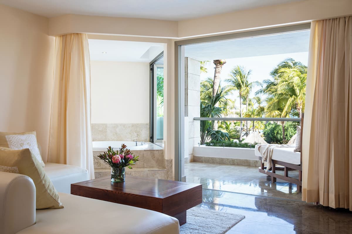 A modern hotel room with a balcony, a sofa, a coffee table, and a view of palm trees.