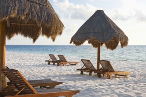 A beach with wooden lounge chairs and thatched umbrellas. - Excellence Playa Mujeres - Adults Only All Inclusive (Punta Sam)