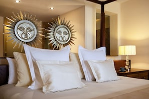 A hotel room with a large bed, multiple pillows, a nightstand with a lamp, and two sunburst wall decorations.
