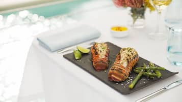 A dining table with a black slate serving board holding a lobster tail and asparagus, accompanied by a knife and a small bowl of sauce.