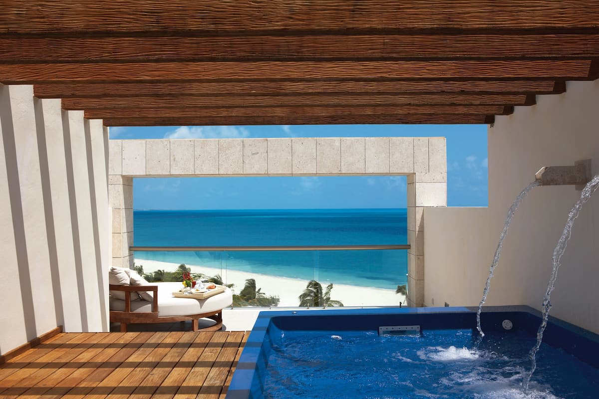 A balcony with a wooden floor, a hot tub, and a view of the beach.