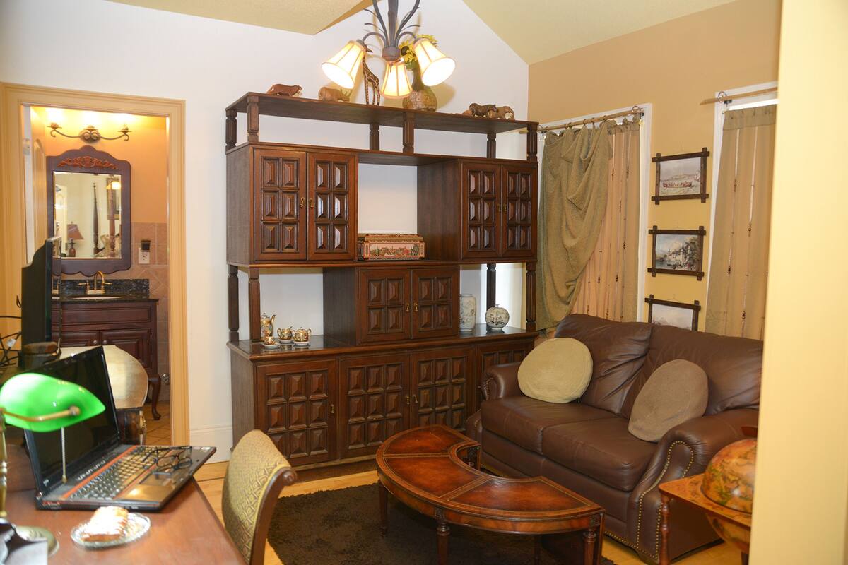 A living room with a brown leather sofa, a wooden cabinet, and a laptop on a table.