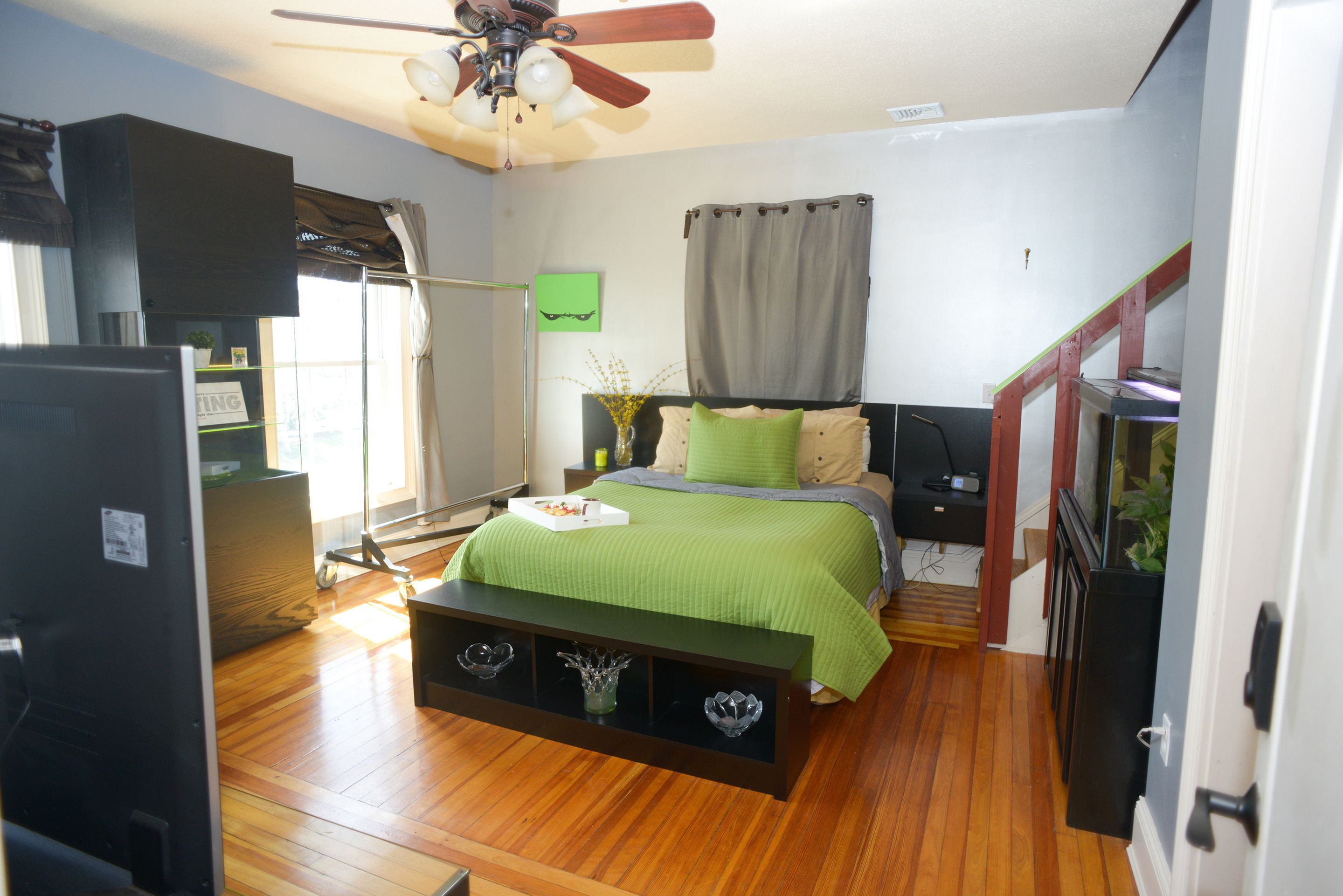 A bedroom with a bed, a nightstand, a dresser, a ceiling fan, and a window with curtains.