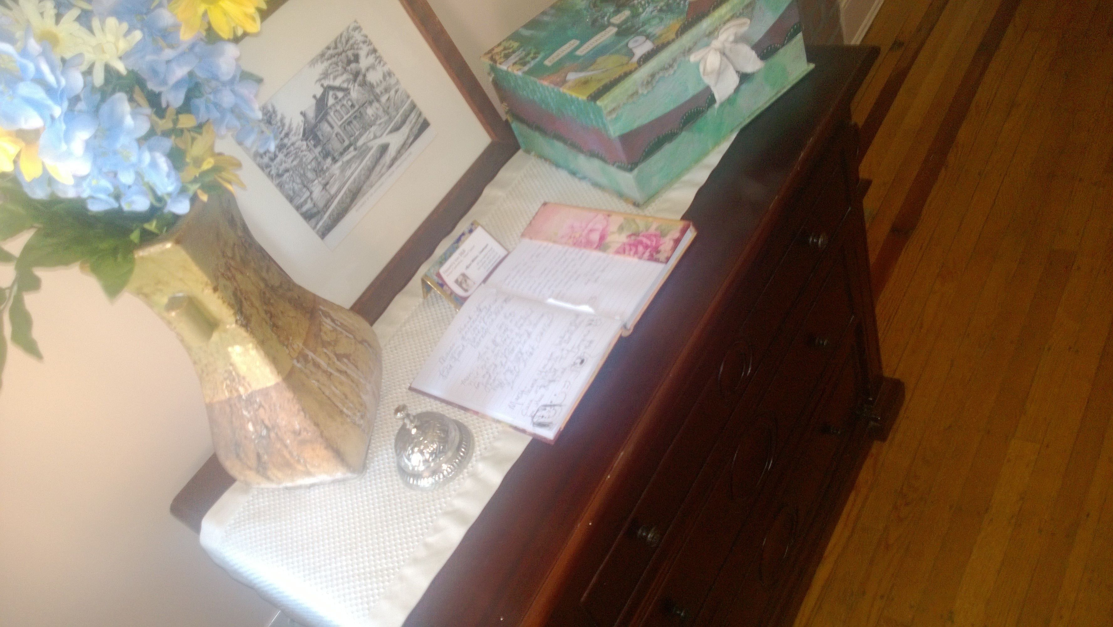 Een bureau met een bloevas, een ingelijst beeld, een stapel boeken en een notitieboek.