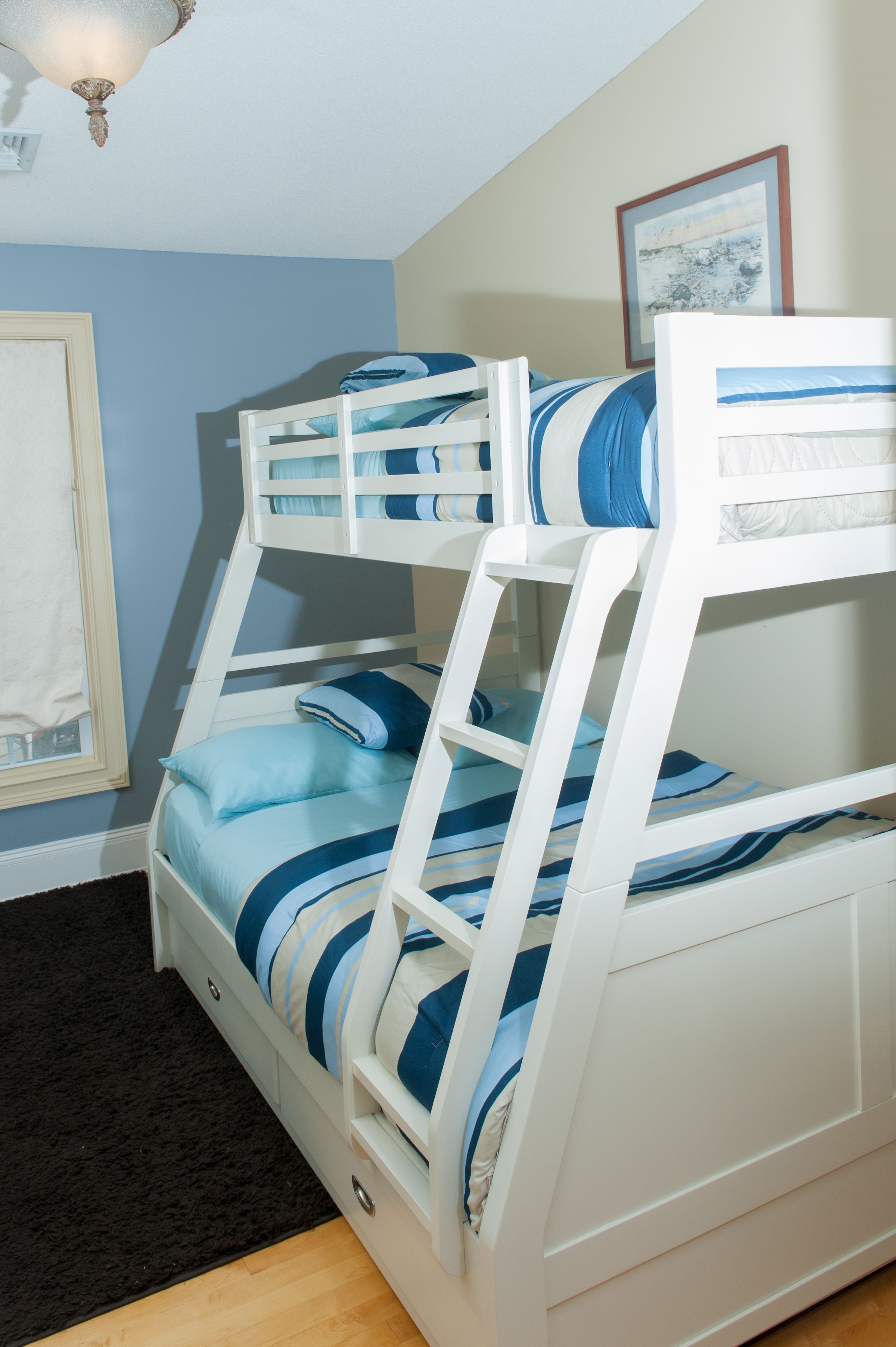Una cama litera con ropa de cama azul y blanca, una alfombra negra y un cuadro en la pared.