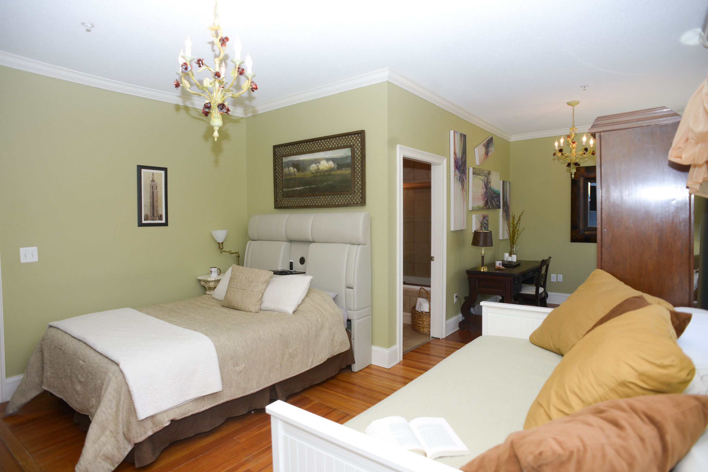 A bedroom with a double bed, a bedside table, a chair, and a desk. There is a chandelier hanging from the ceiling.