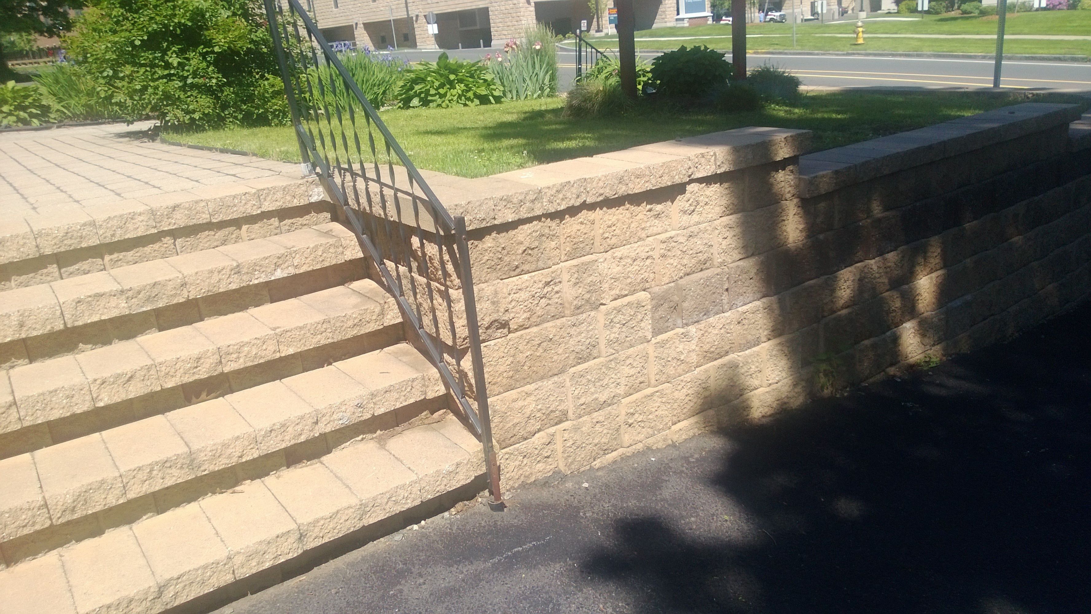 A set of stone steps with a metal handrail leading to a brick wall.