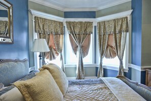 A bedroom with a bed, a nightstand, a lamp, and a window with curtains.