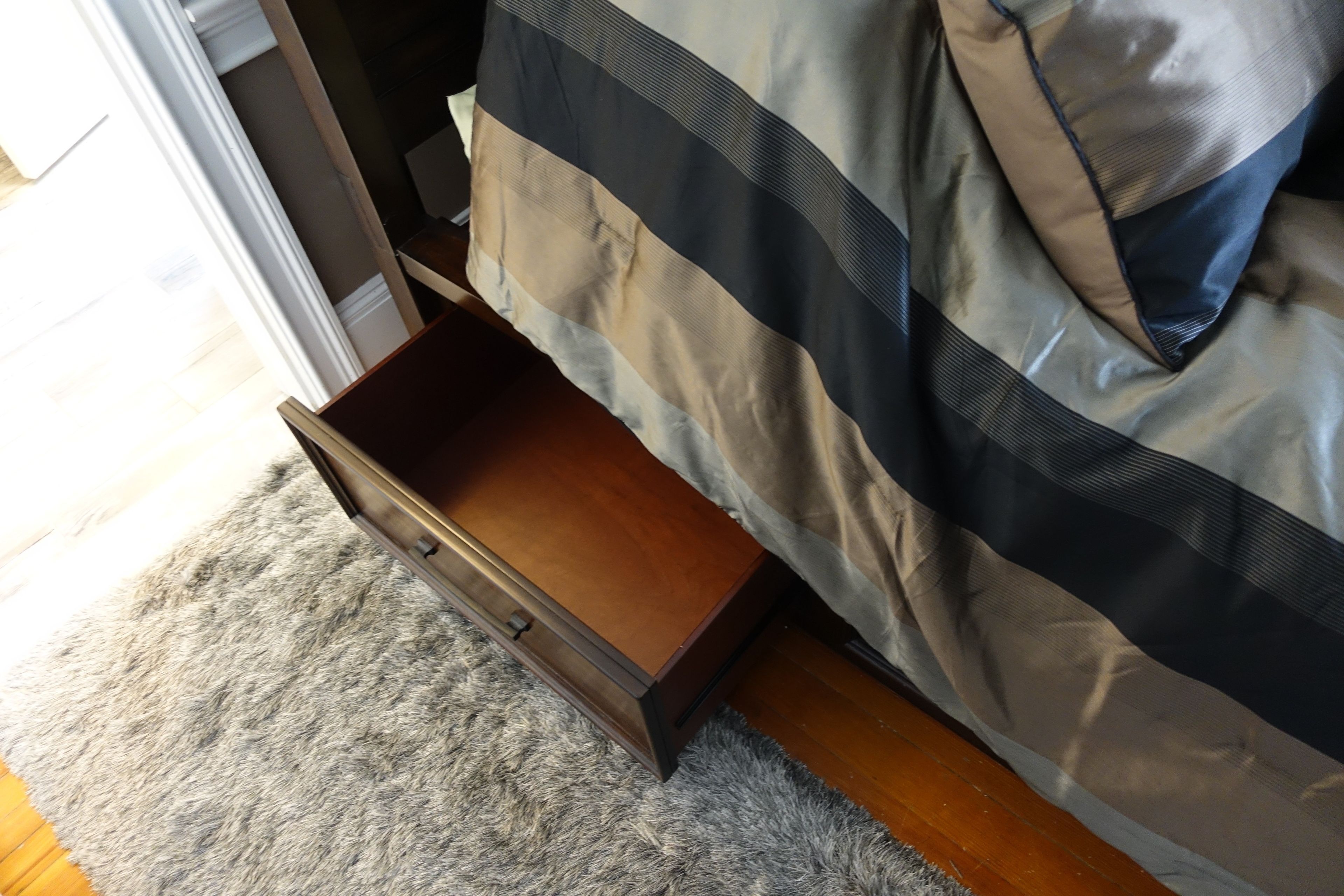 A bedroom with a wooden drawer under the bed, a grey carpet, and a bed with a striped blanket.