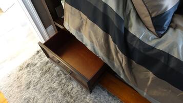 A bedroom with a wooden drawer under the bed, a grey carpet, and a bed with a striped blanket.