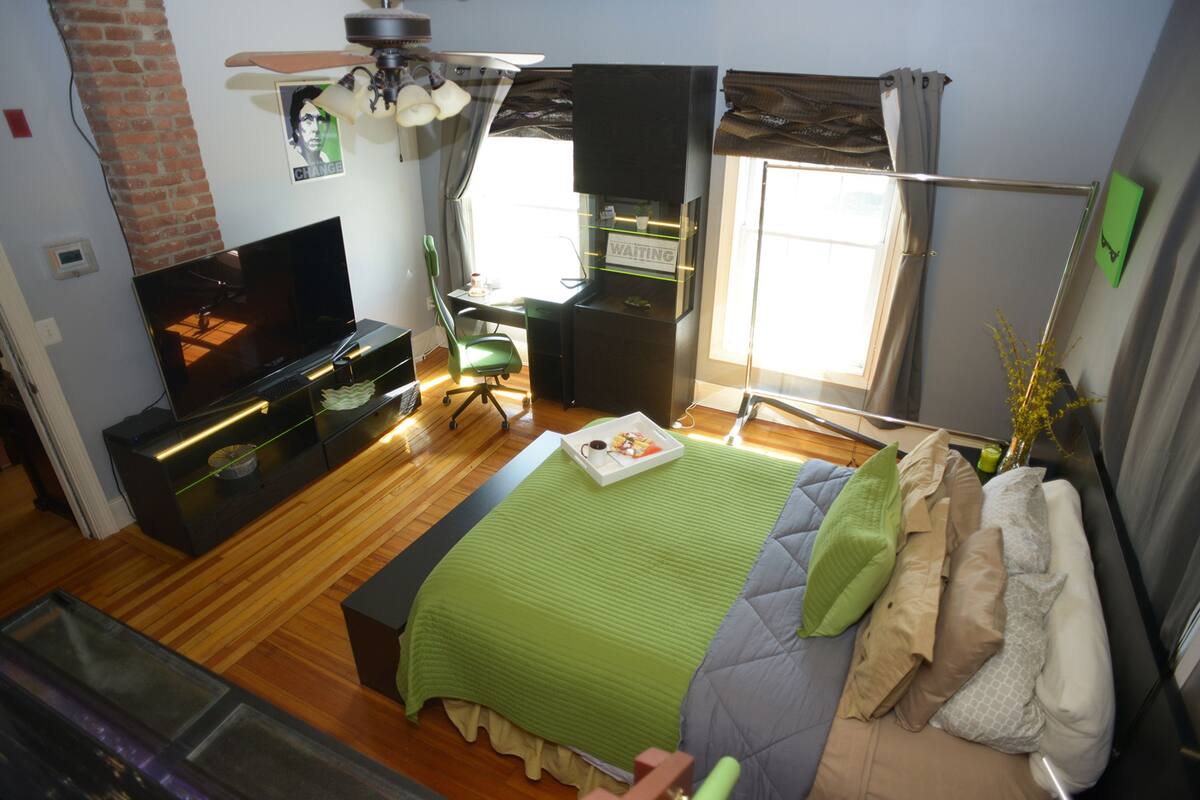 A modern bedroom with a TV, a desk, a chair, a bed with multiple pillows, and a window with curtains.
