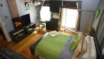 A modern bedroom with a TV, a desk, a chair, a bed with multiple pillows, and a window with curtains.