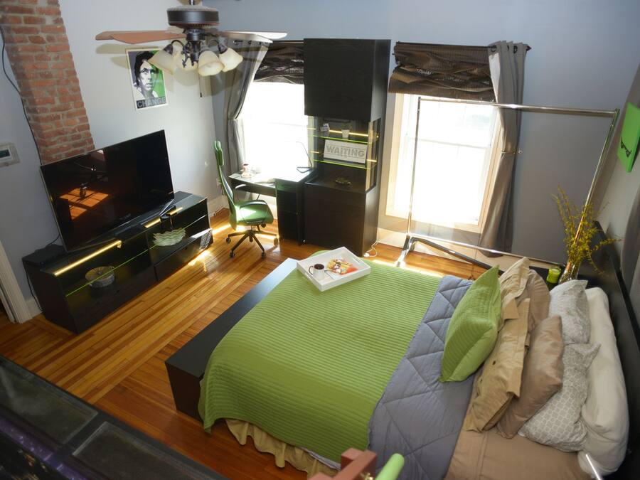 A modern bedroom with a TV, a desk, a chair, a bed with multiple pillows, and a window with curtains.
