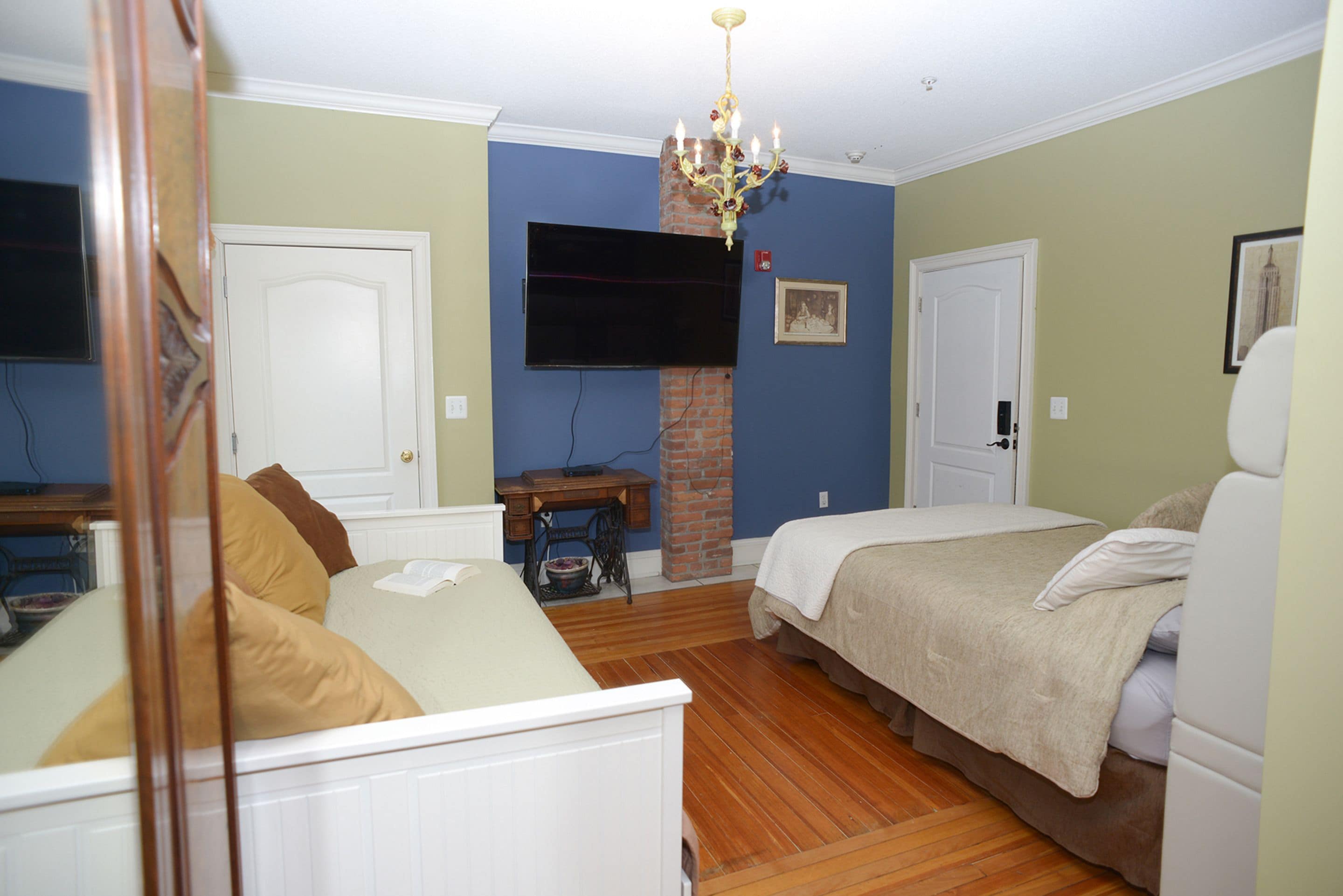 A bedroom with a bed, a dresser, a chair, a television mounted on the wall, and a chandelier.