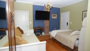 A bedroom with a bed, a dresser, a chair, a television mounted on the wall, and a chandelier.