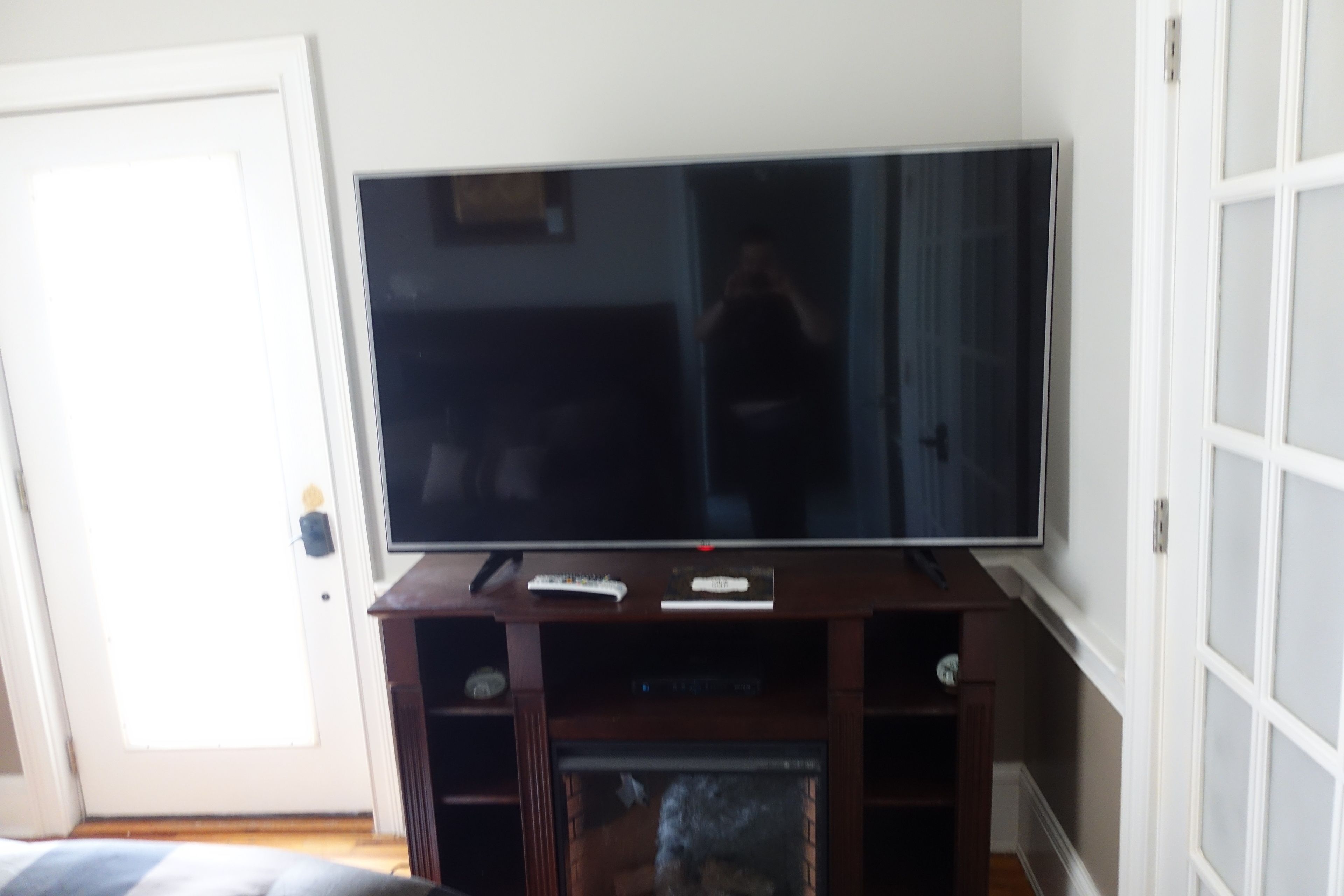 A flat-screen TV on a wooden stand with a remote control and a small shelf below.
