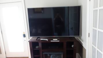 A flat-screen TV on a wooden stand with a remote control and a small shelf below.