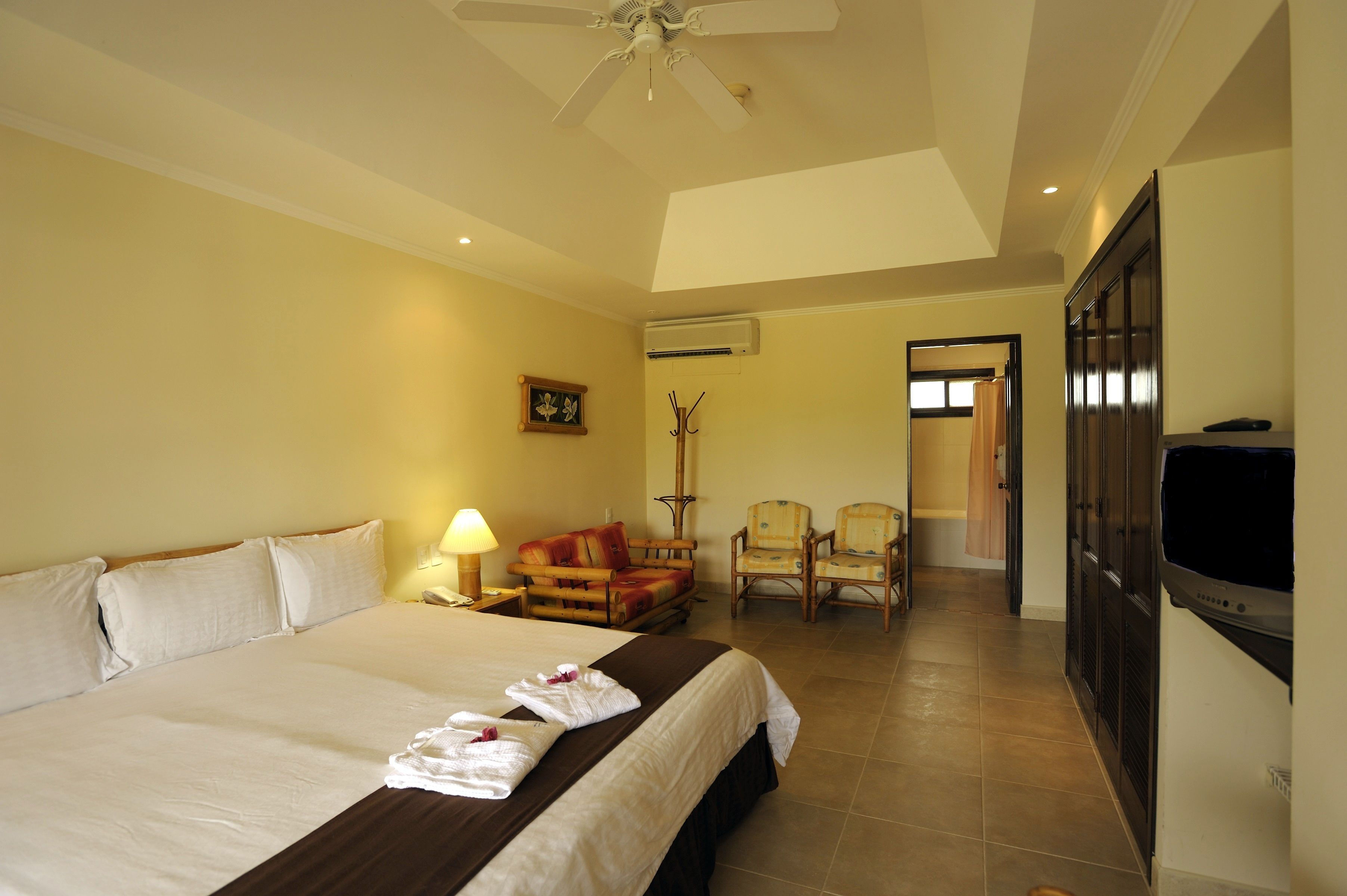 A hotel room with a large bed, a ceiling fan, a TV, and a seating area with chairs.