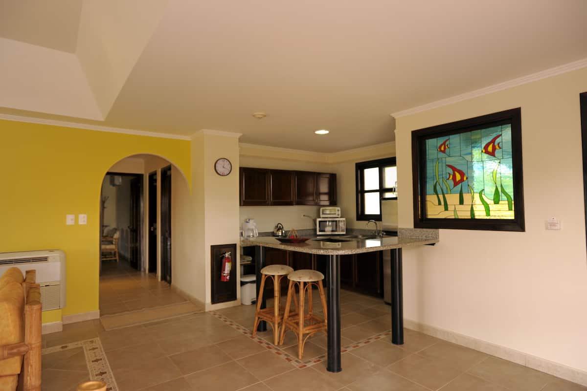 A kitchen with a central island, stools, a clock, and a decorative fish window.