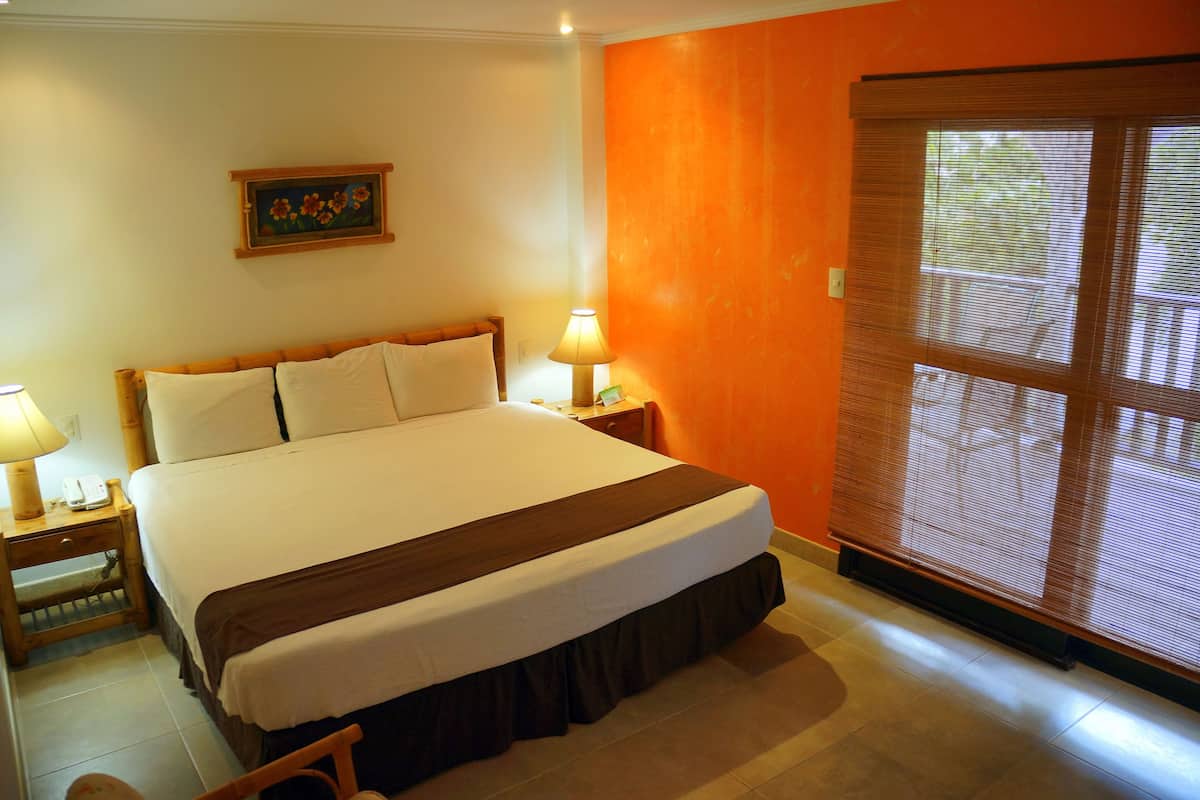 A hotel room with a large bed, two bedside lamps, a nightstand, and a window with blinds.
