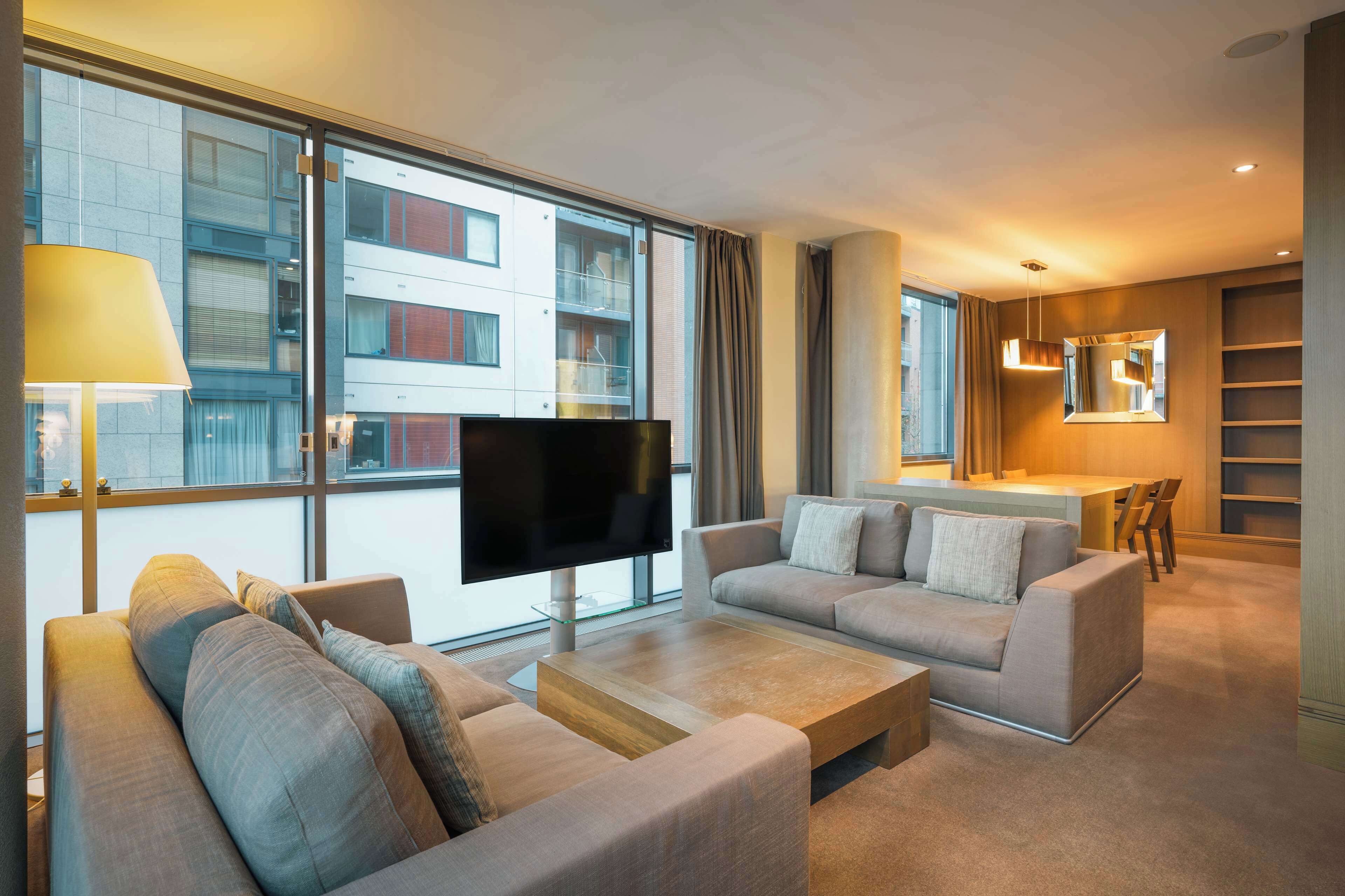 A modern living room with a flat-screen TV, two sofas, a coffee table, and a dining area with a small table and chairs.
