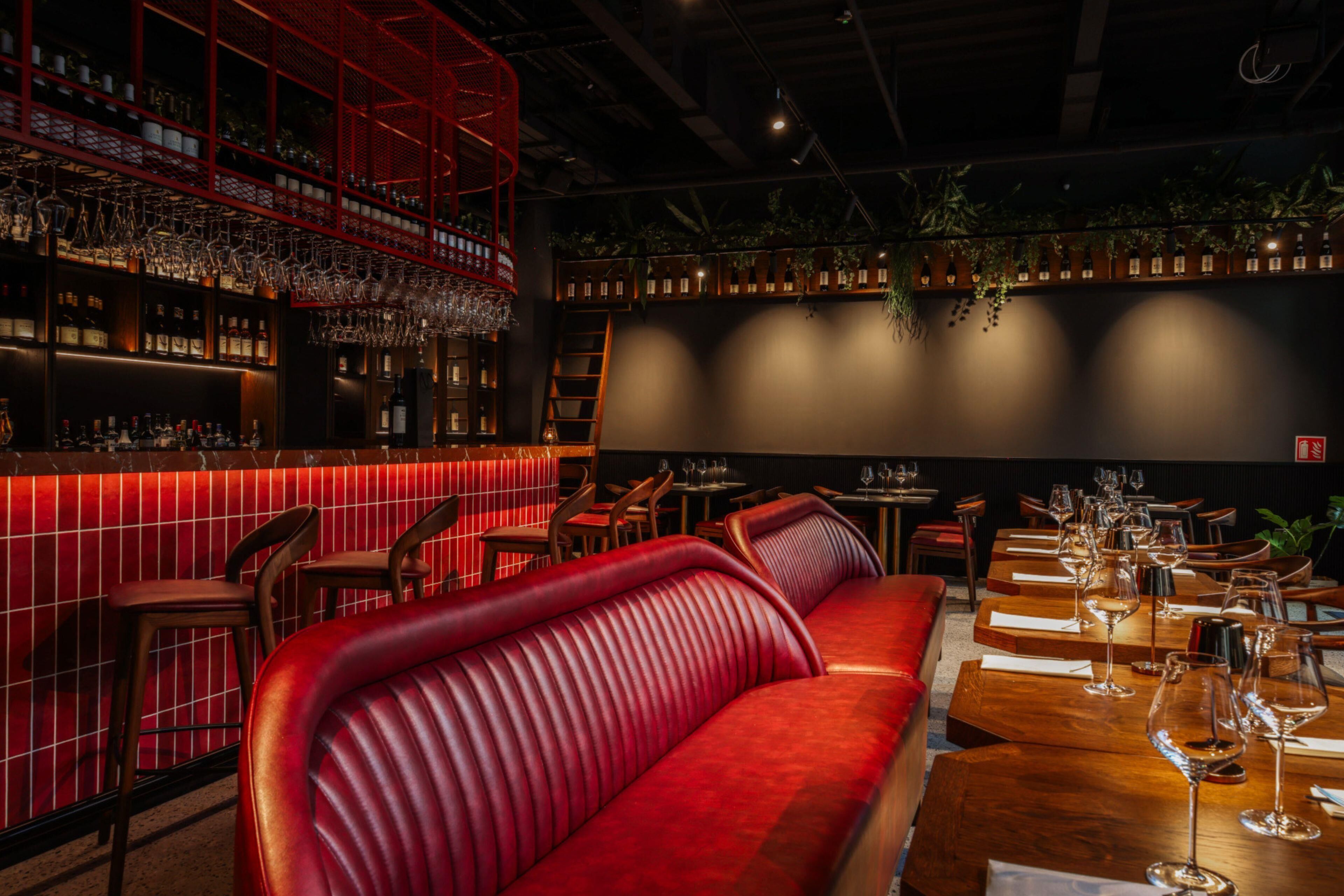 A bar area with a red seating area, wooden tables, and a variety of bottles and glasses.