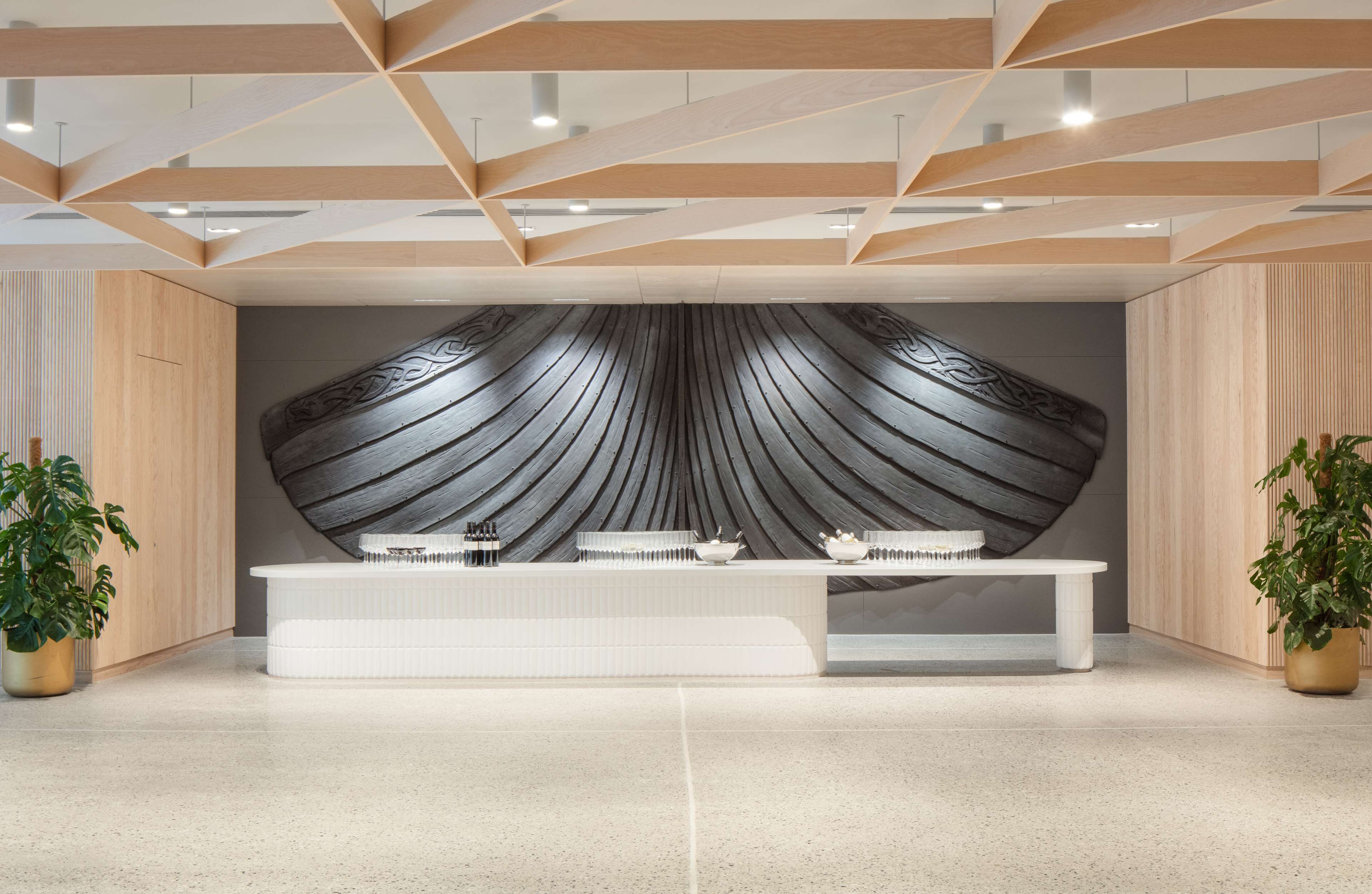 A reception area with a modern design, featuring a central white reception desk, a patterned wall, and wooden ceiling beams.