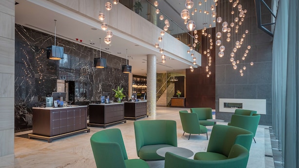 A modern lobby with marble walls, a reception desk, green seating, and a staircase. - Radisson Blu Royal Hotel, Dublin (Dublin)